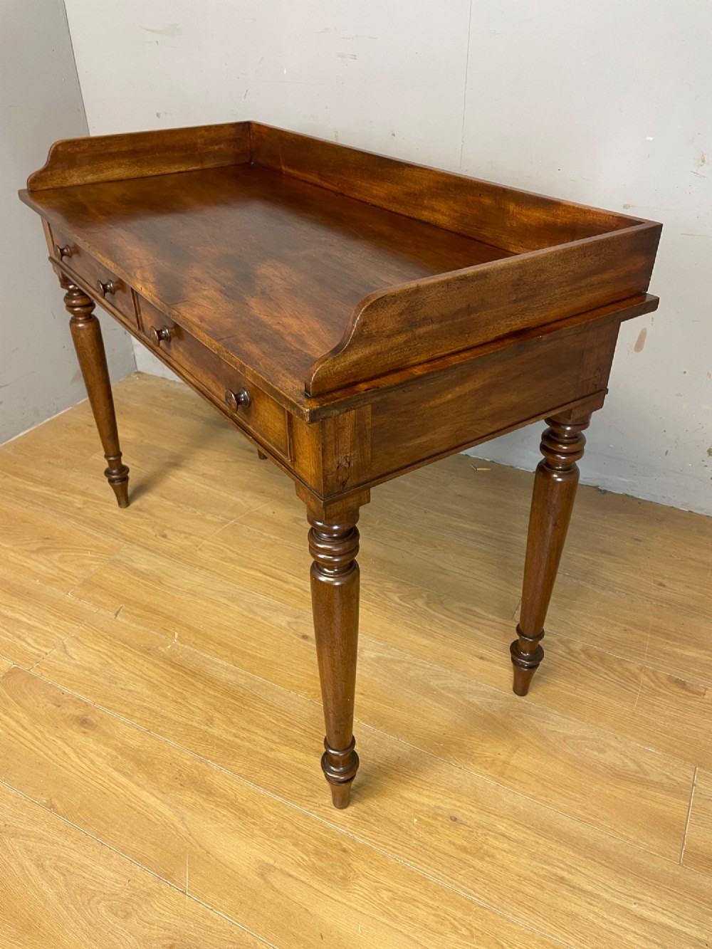 A nineteenth-century flame mahogany side table featuring a three-sided gallery top, two inline drawers with turned knobs, and four turned legs. View VIII