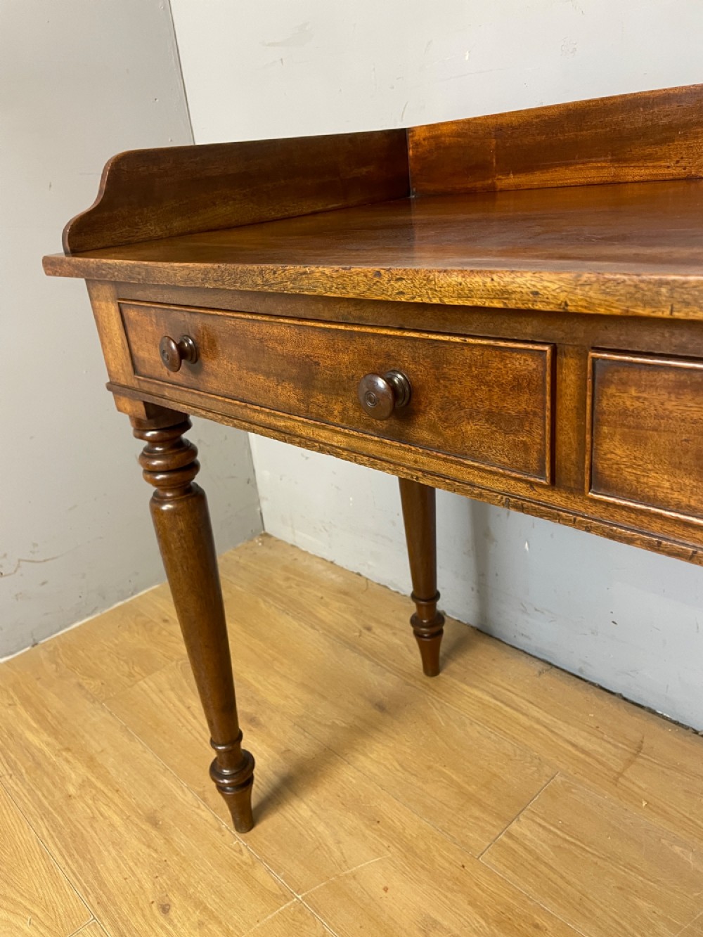 A nineteenth-century flame mahogany side table featuring a three-sided gallery top, two inline drawers with turned knobs, and four turned legs. View X