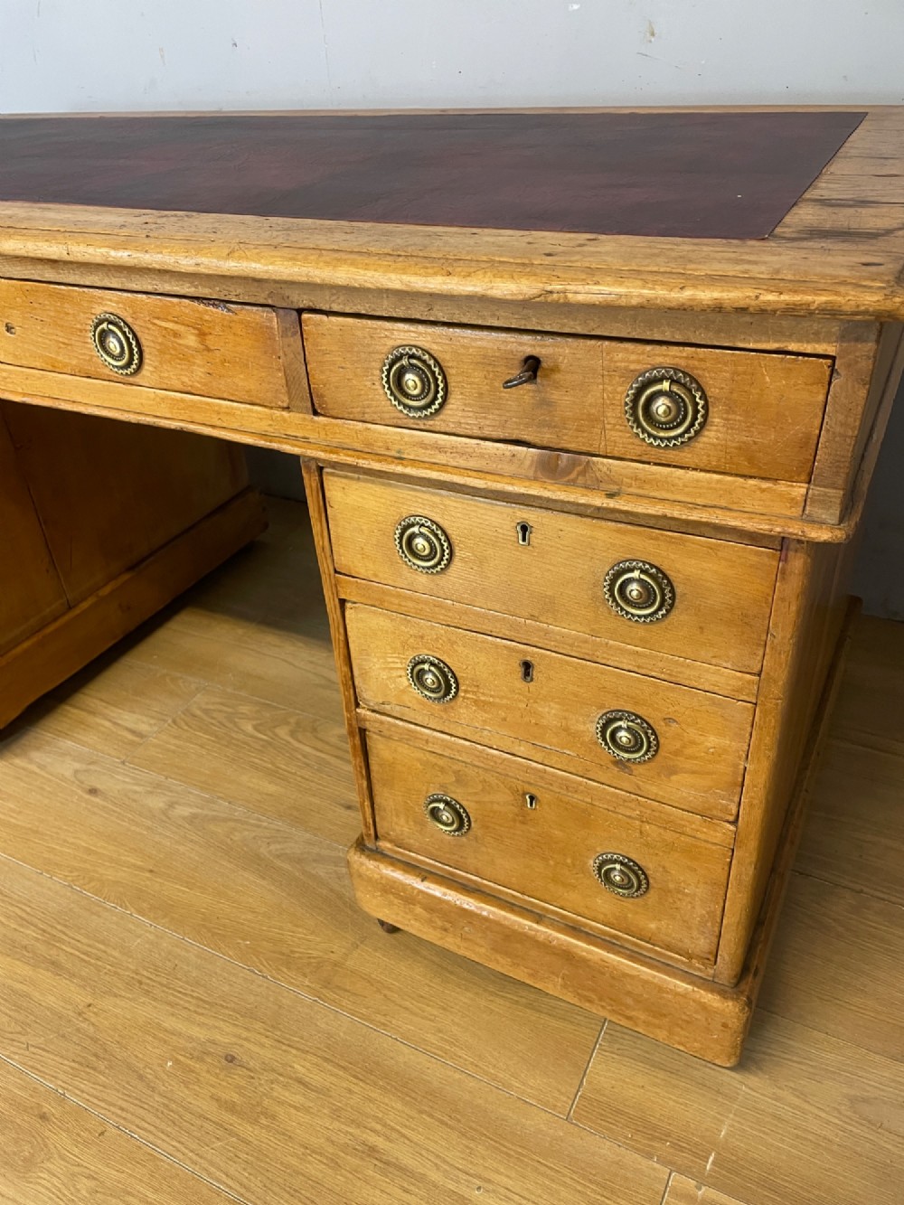 A Victorian three-part pine twin pedestal desk featuring a burgundy leather writing inset, multiple brass ring-pull drawers, and a plinth base. View VI