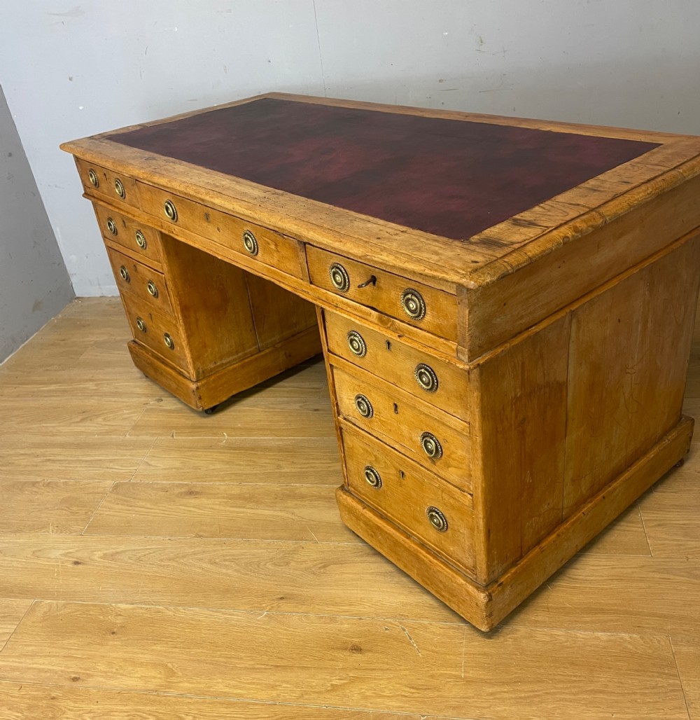 A Victorian three-part pine twin pedestal desk featuring a burgundy leather writing inset, multiple brass ring-pull drawers, and a plinth base. View VIII