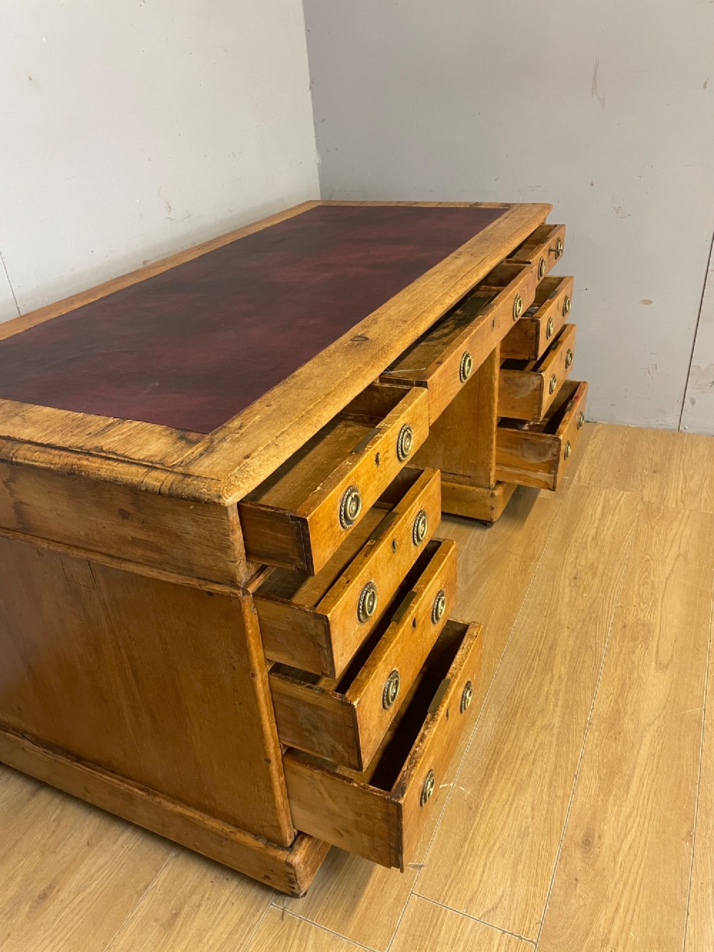 A Victorian three-part pine twin pedestal desk featuring a burgundy leather writing inset, multiple brass ring-pull drawers, and a plinth base. View IX