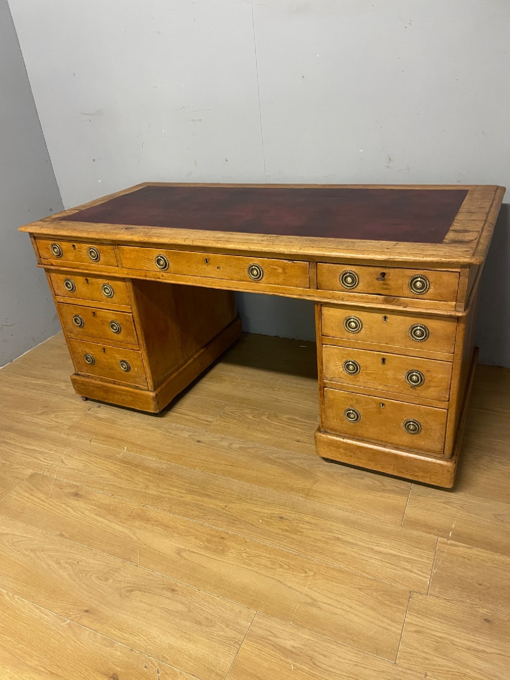 A Victorian three-part pine twin pedestal desk featuring a burgundy leather writing inset, multiple brass ring-pull drawers, and a plinth base. View XIII
