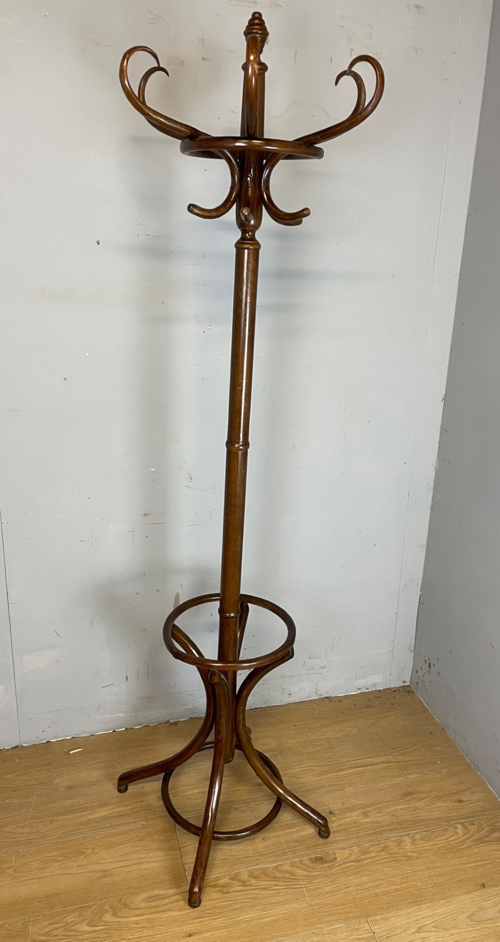 A tall dark brown bentwood freestanding coat and stick stand featuring curved upper hooks and a circular umbrella holder base.