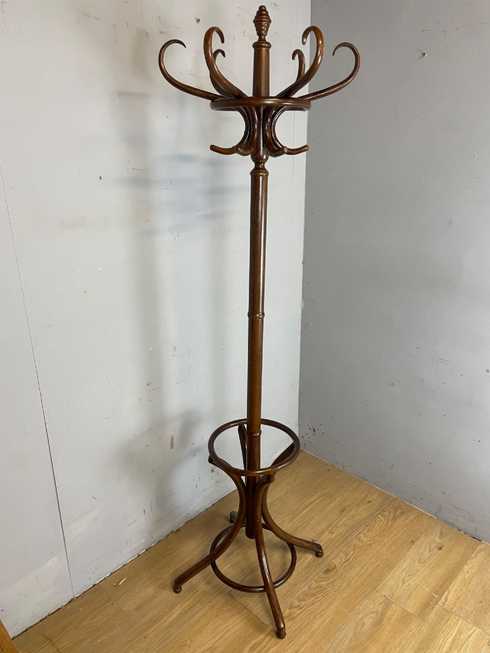 A tall dark brown bentwood freestanding coat and stick stand featuring curved upper hooks and a circular umbrella holder base. View II