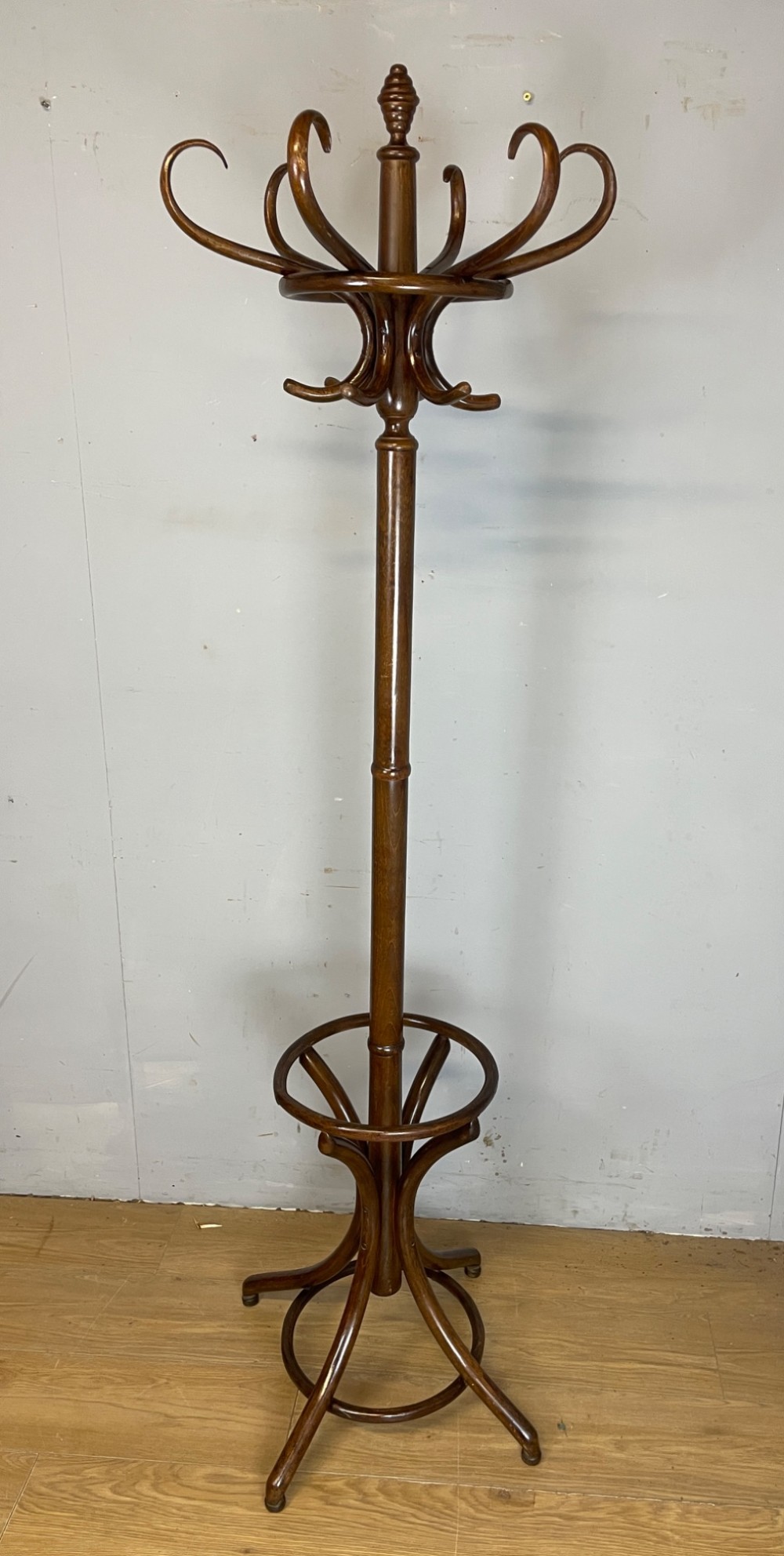A tall dark brown bentwood freestanding coat and stick stand featuring curved upper hooks and a circular umbrella holder base. View V