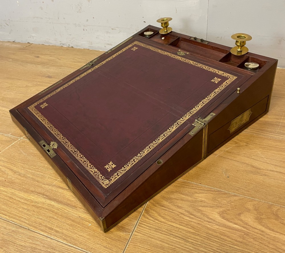 A 19th-century mahogany campaign writing slope featuring brass corner mounts, candle holders, and a gold-tooled burgundy leather writing surface.