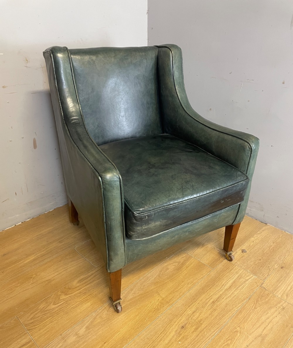 An Edwardian green leather armchair with sloping sides, a square seat cushion, and square tapered mahogany legs fitted with brass castors. View II