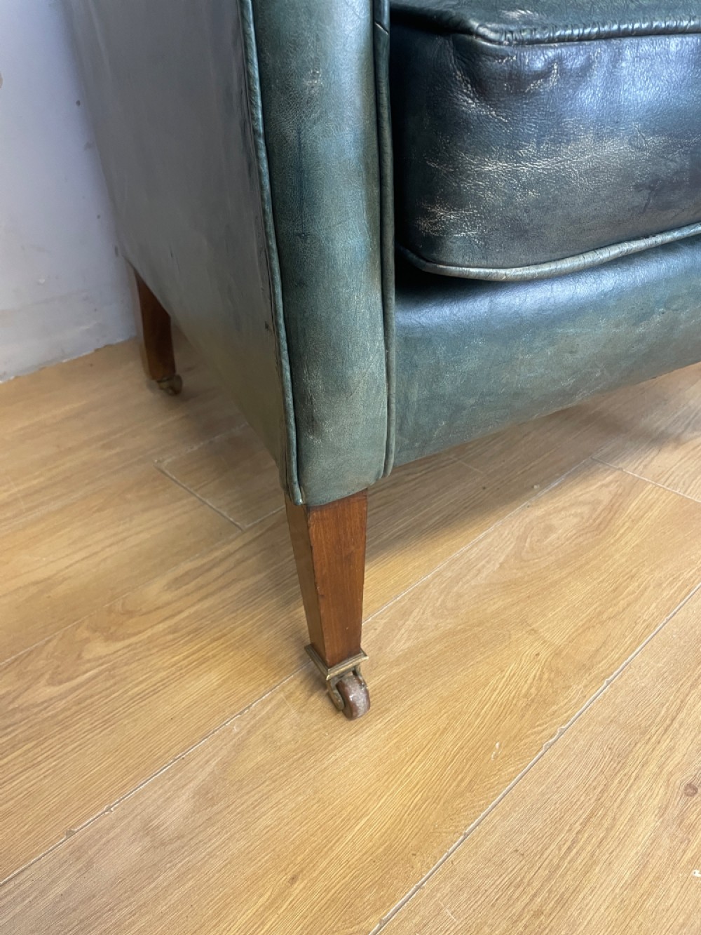 An Edwardian green leather armchair with sloping sides, a square seat cushion, and square tapered mahogany legs fitted with brass castors. View III