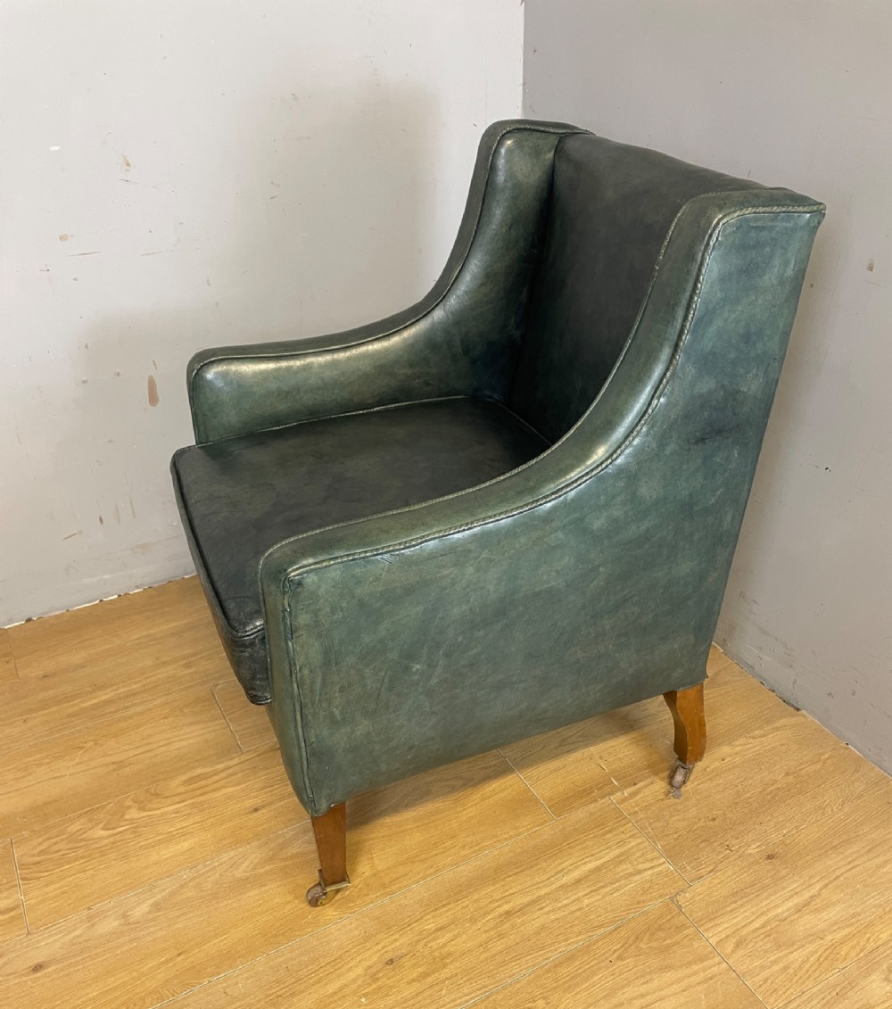 An Edwardian green leather armchair with sloping sides, a square seat cushion, and square tapered mahogany legs fitted with brass castors. View IV