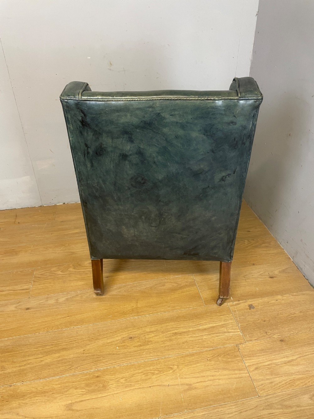 An Edwardian green leather armchair with sloping sides, a square seat cushion, and square tapered mahogany legs fitted with brass castors. View V