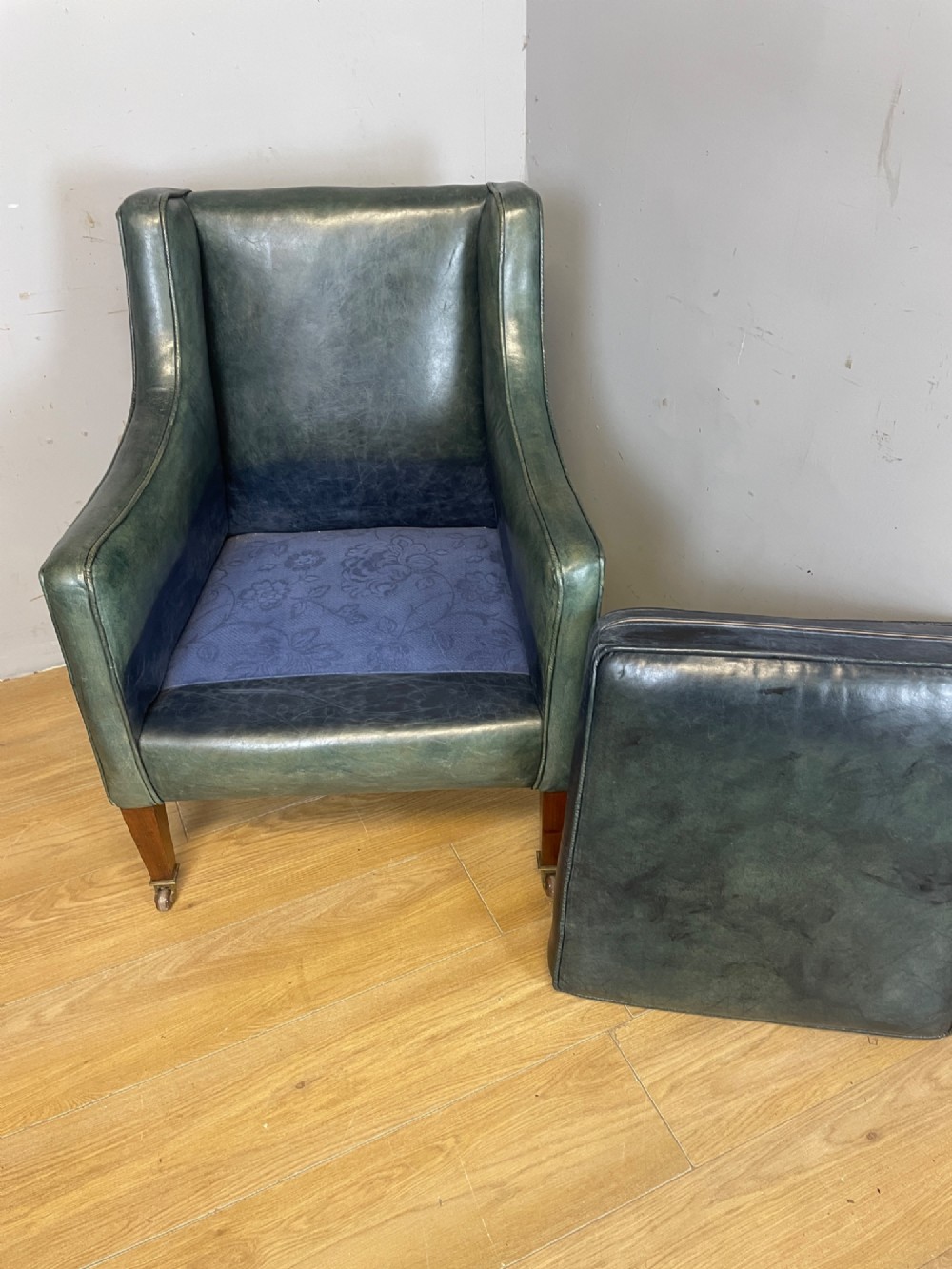 An Edwardian green leather armchair with sloping sides, a square seat cushion, and square tapered mahogany legs fitted with brass castors. View VI