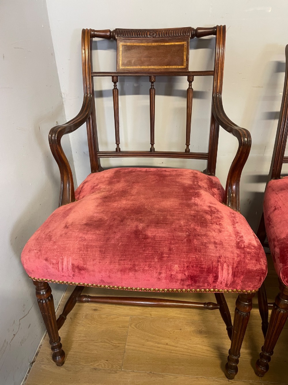 A set of ten nineteenth-century mahogany dining chairs featuring rectangular inlaid backrests, spindle uprights, and red velvet upholstered seats with brass stud detailing. View V