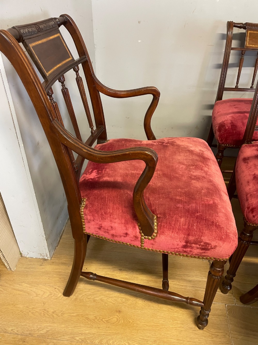 A set of ten nineteenth-century mahogany dining chairs featuring rectangular inlaid backrests, spindle uprights, and red velvet upholstered seats with brass stud detailing. View VII
