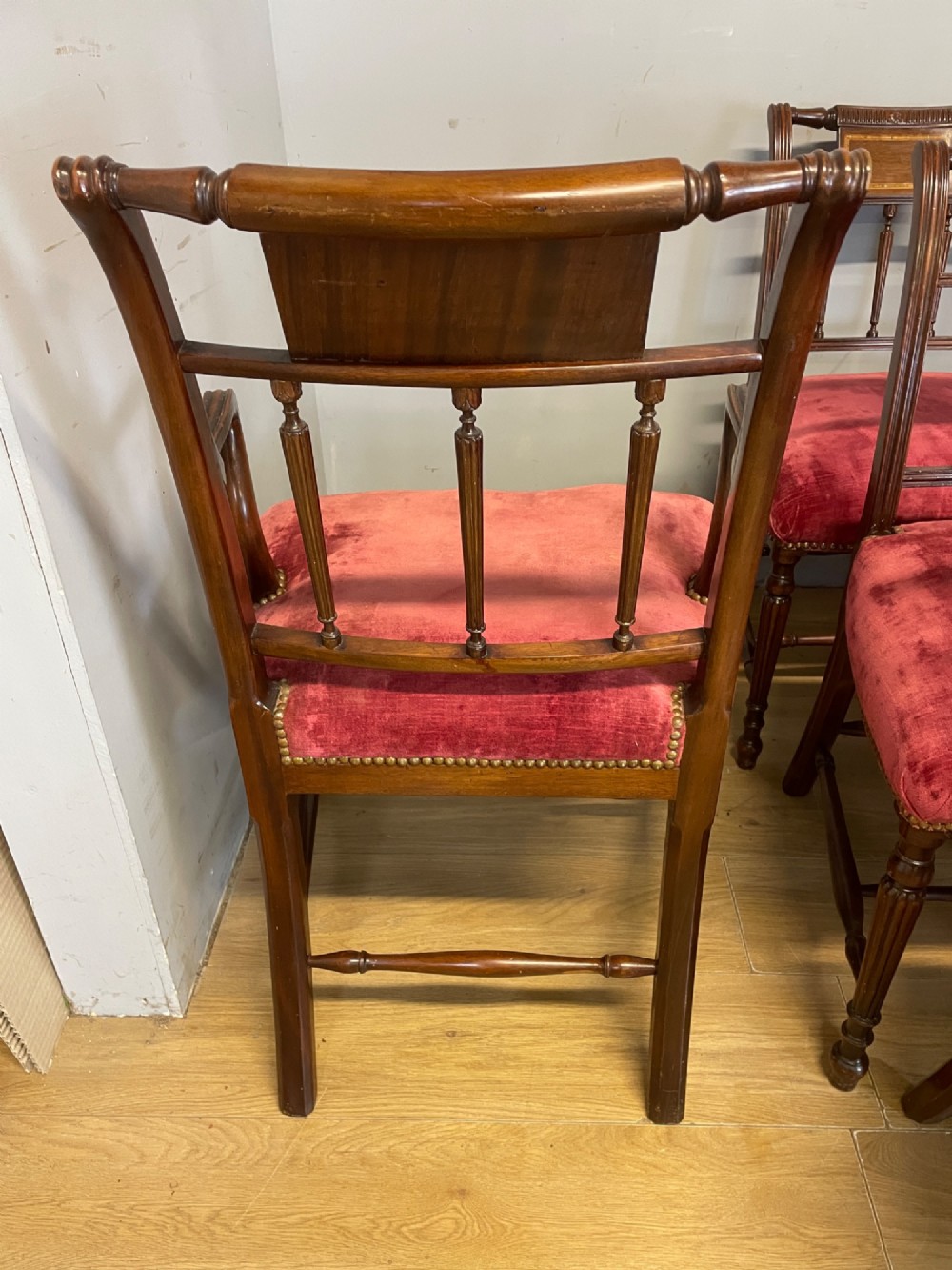 A set of ten nineteenth-century mahogany dining chairs featuring rectangular inlaid backrests, spindle uprights, and red velvet upholstered seats with brass stud detailing. View VIII