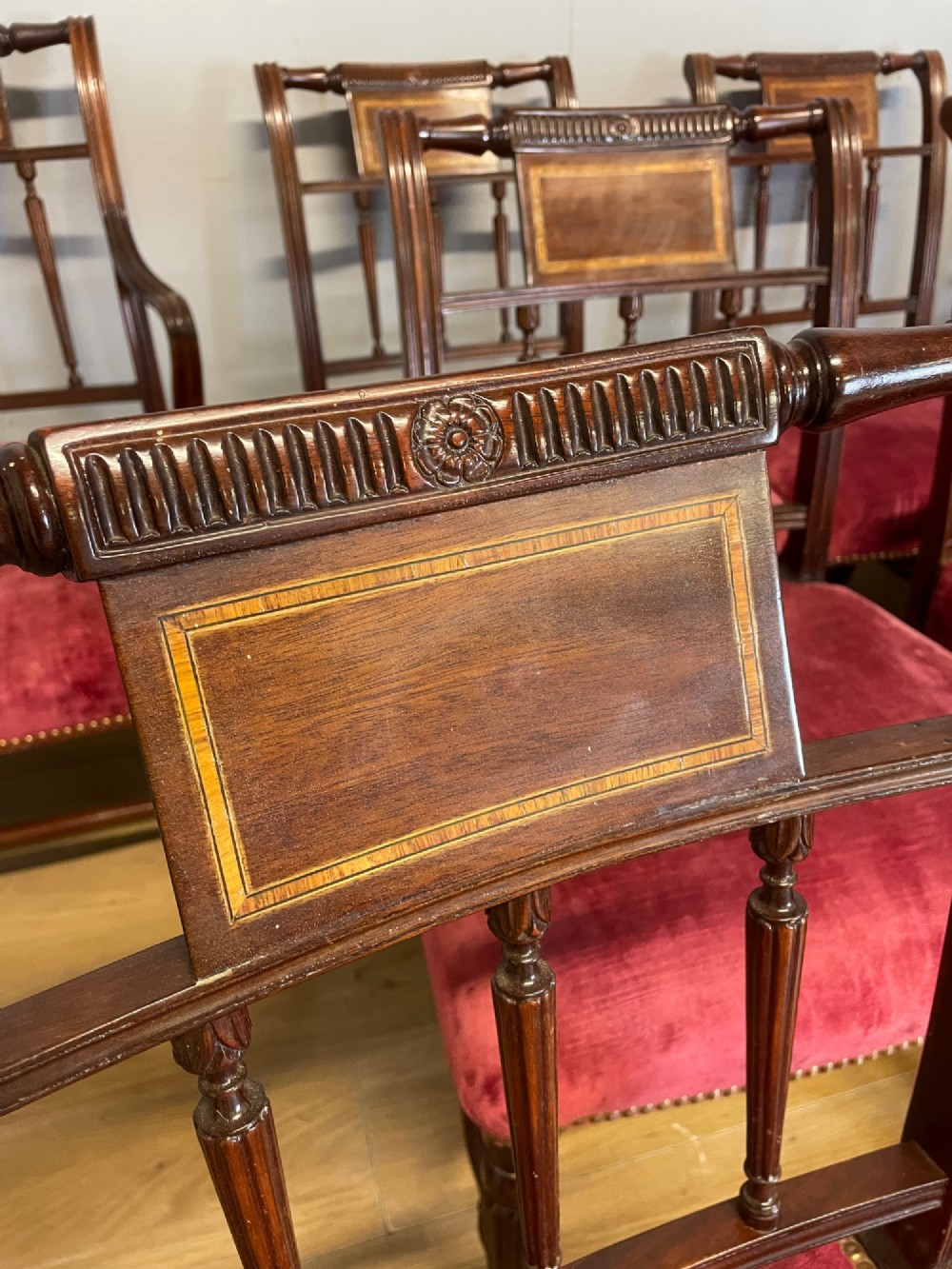 A set of ten nineteenth-century mahogany dining chairs featuring rectangular inlaid backrests, spindle uprights, and red velvet upholstered seats with brass stud detailing. View XI