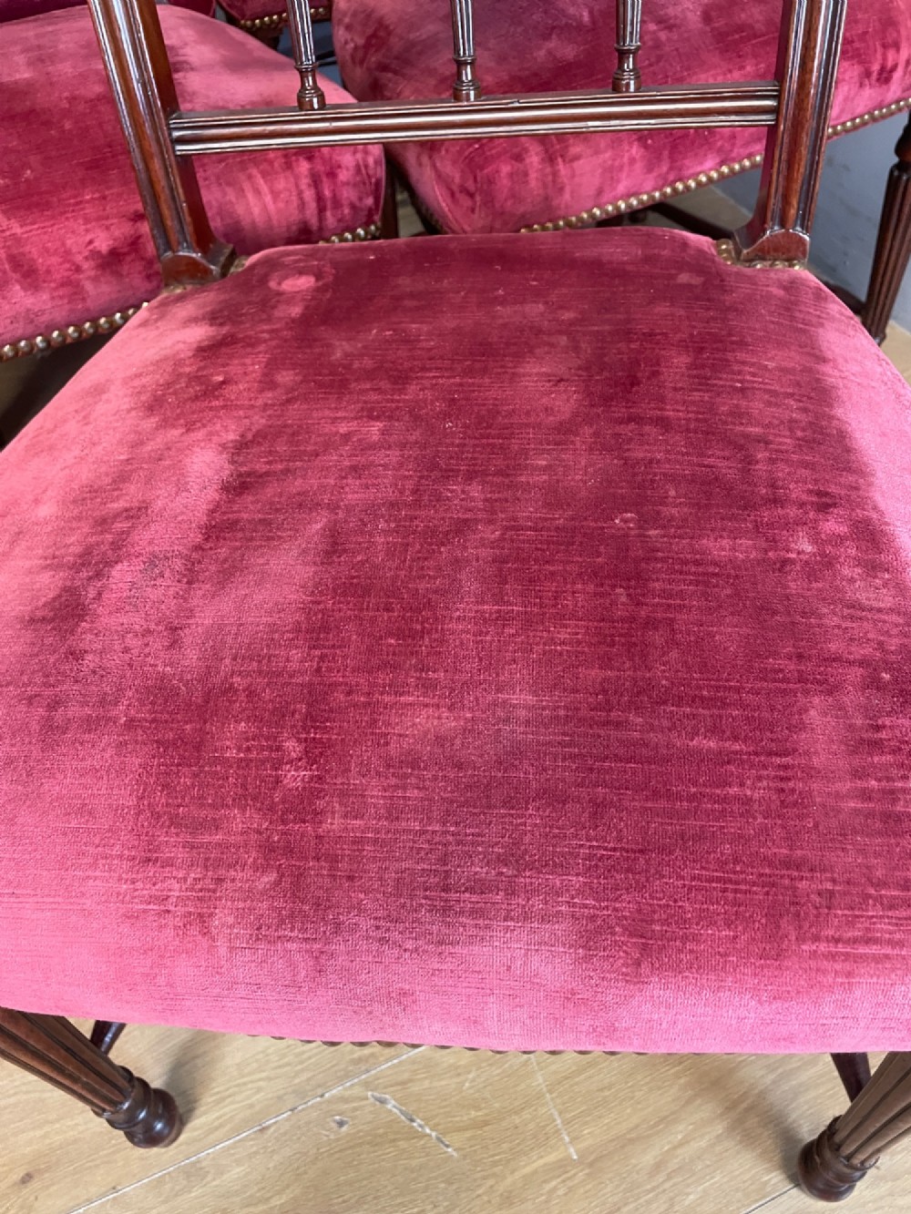 A set of ten nineteenth-century mahogany dining chairs featuring rectangular inlaid backrests, spindle uprights, and red velvet upholstered seats with brass stud detailing. View XIV