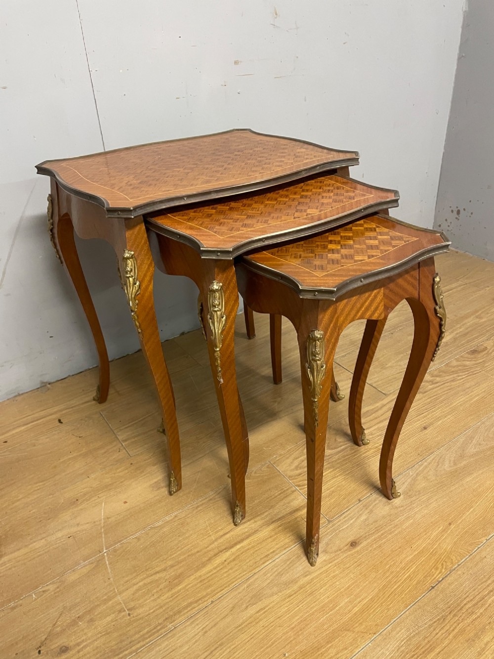 A set of three graduated French kingwood nesting tables featuring parquetry inlaid tops, cabriole legs, and gilded ormolu mounts.