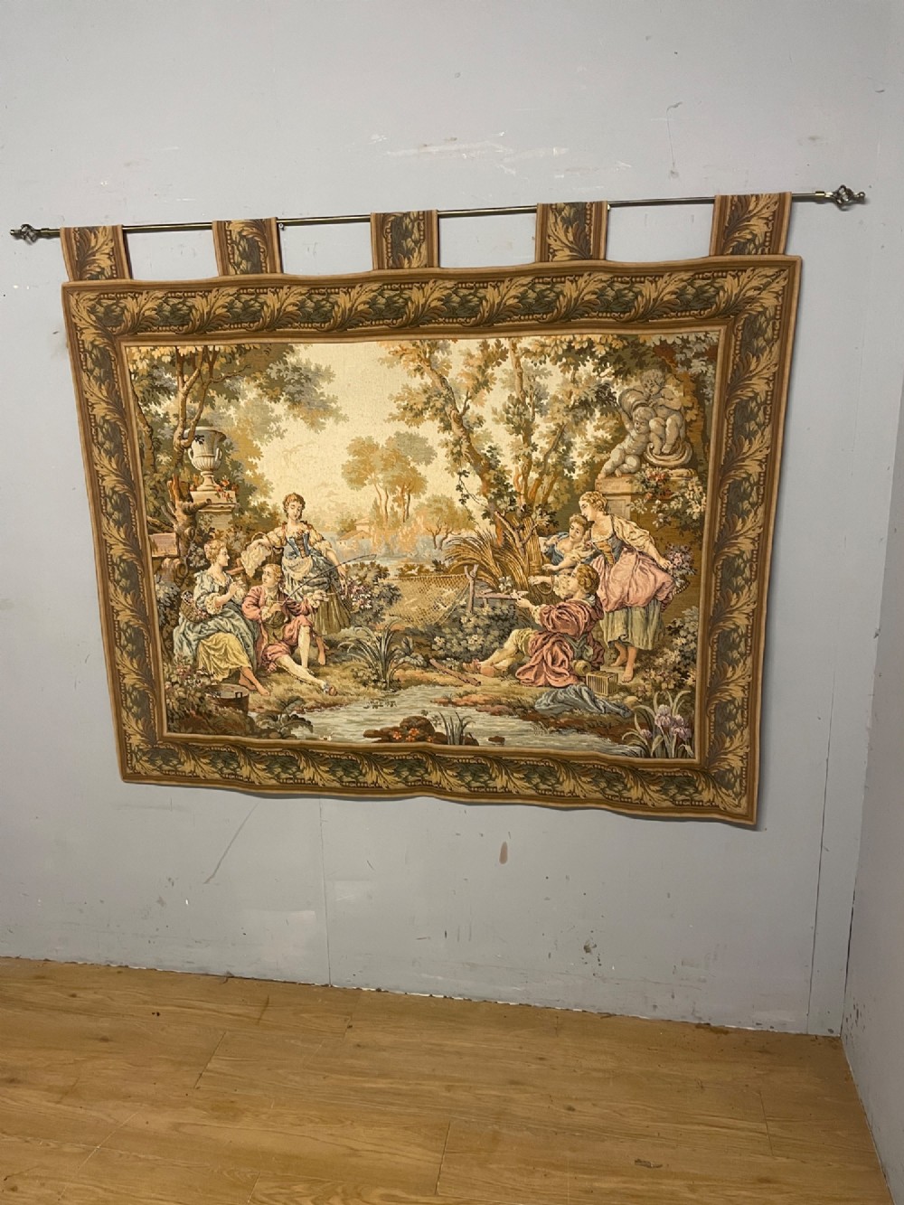 A large woven wall tapestry depicting figures in an 18th-century pastoral landscape with trees, classical sculpture, and a leaf pattern border.