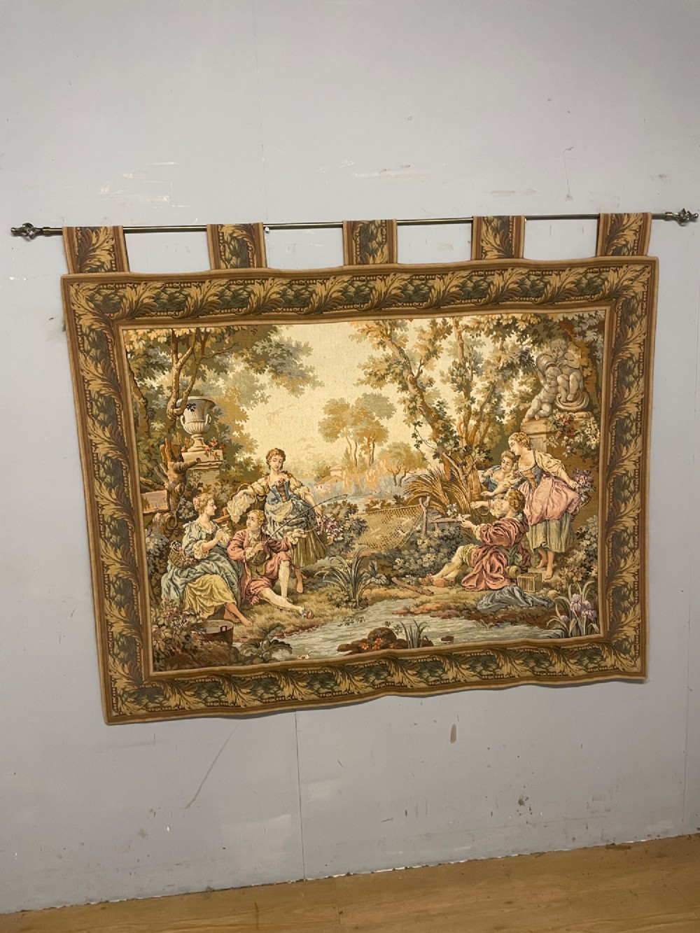 A large woven wall tapestry depicting figures in an 18th-century pastoral landscape with trees, classical sculpture, and a leaf pattern border. View III