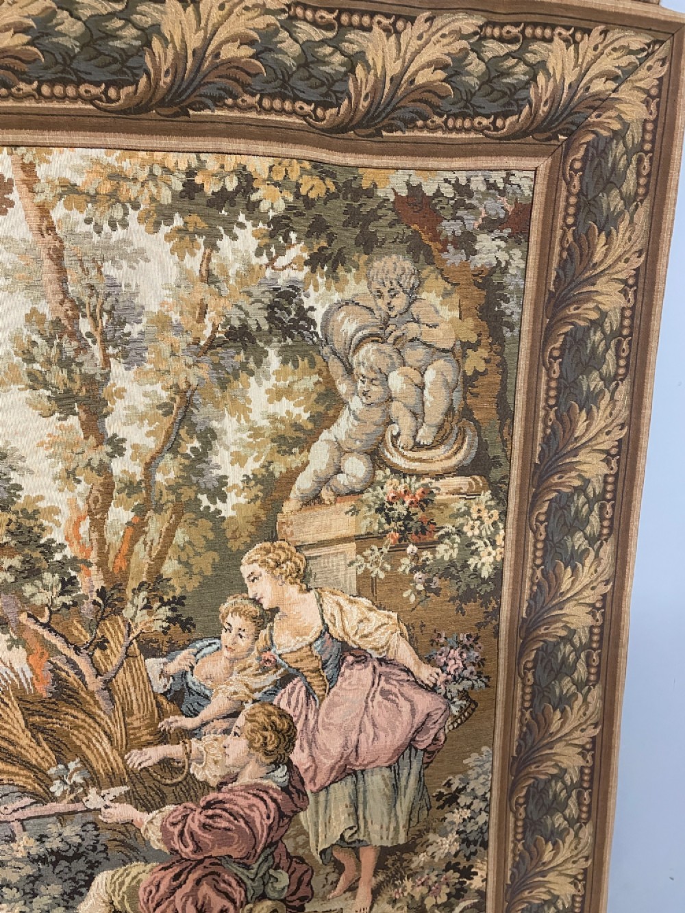 A large woven wall tapestry depicting figures in an 18th-century pastoral landscape with trees, classical sculpture, and a leaf pattern border. View V