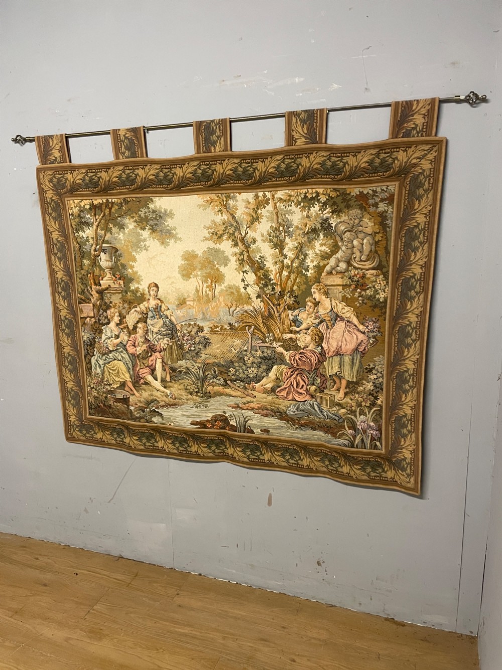 A large woven wall tapestry depicting figures in an 18th-century pastoral landscape with trees, classical sculpture, and a leaf pattern border. View IX