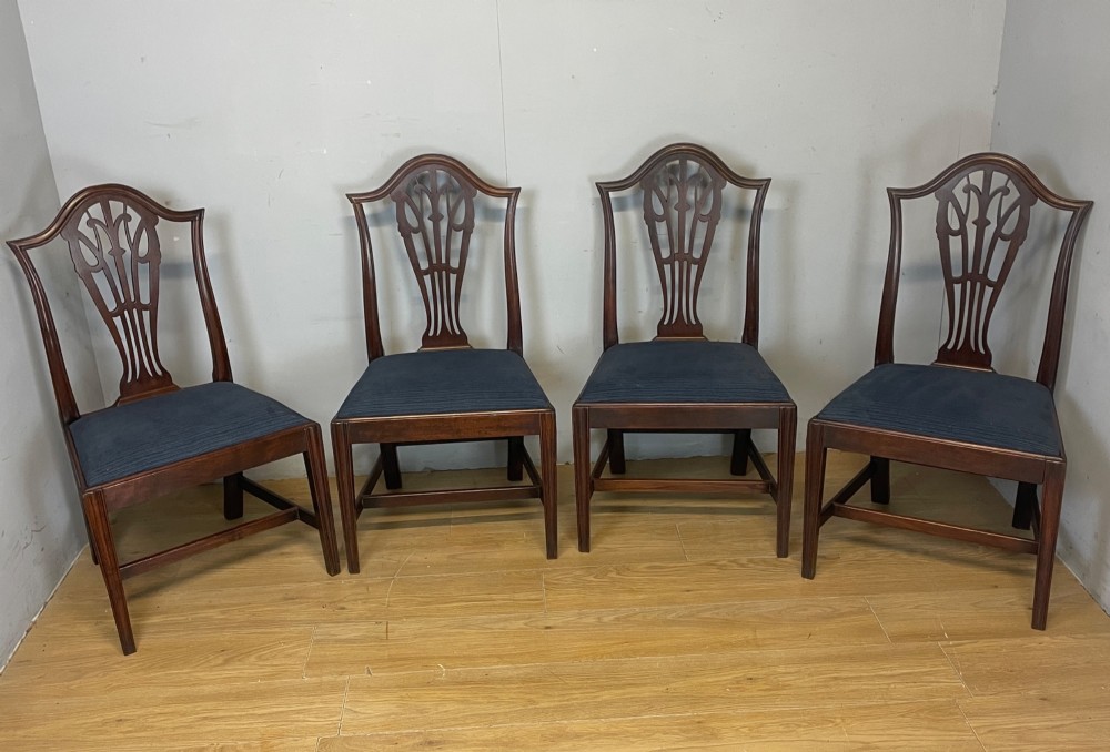 A set of four antique mahogany Chippendale style dining chairs with decorative pierced back splats and dark upholstered seats arranged side by side.