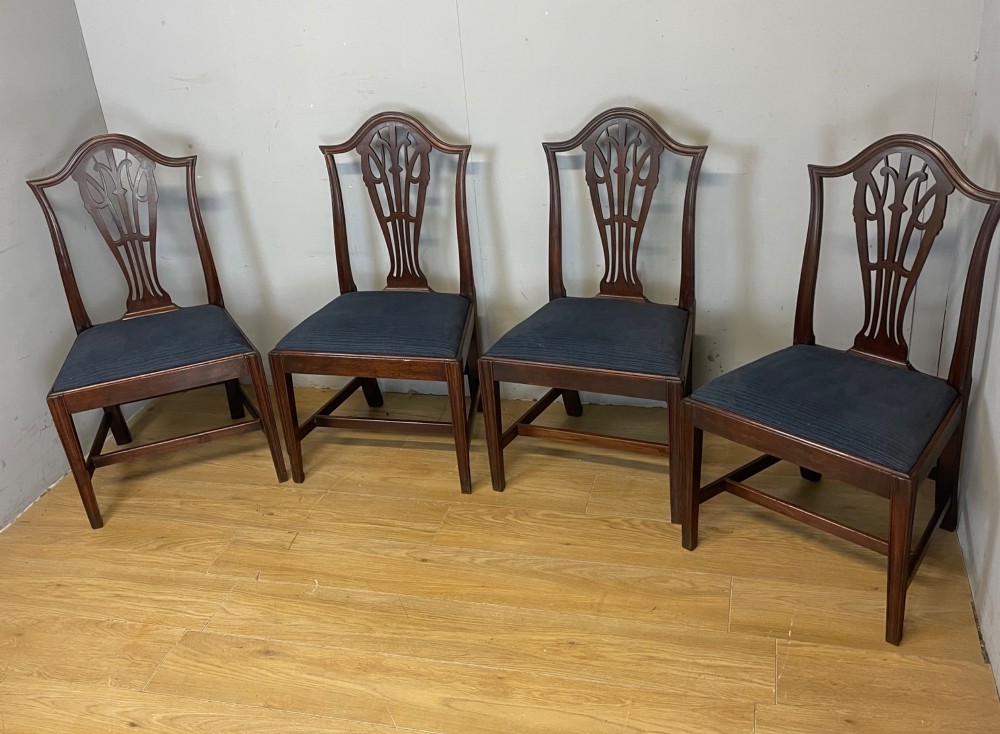 A set of four antique mahogany Chippendale style dining chairs with decorative pierced back splats and dark upholstered seats arranged side by side. View II