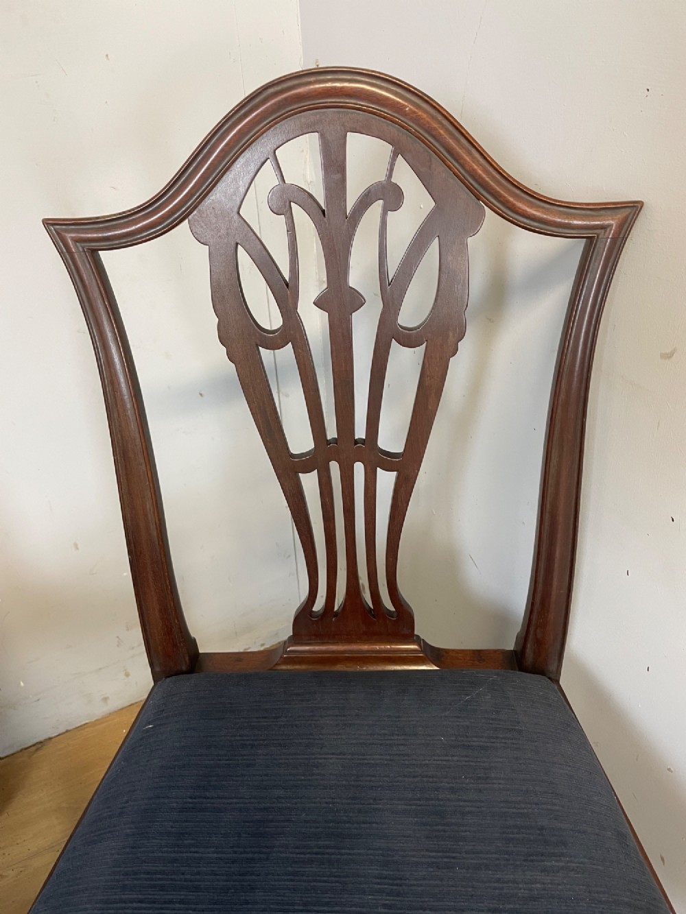 A set of four antique mahogany Chippendale style dining chairs with decorative pierced back splats and dark upholstered seats arranged side by side. View III