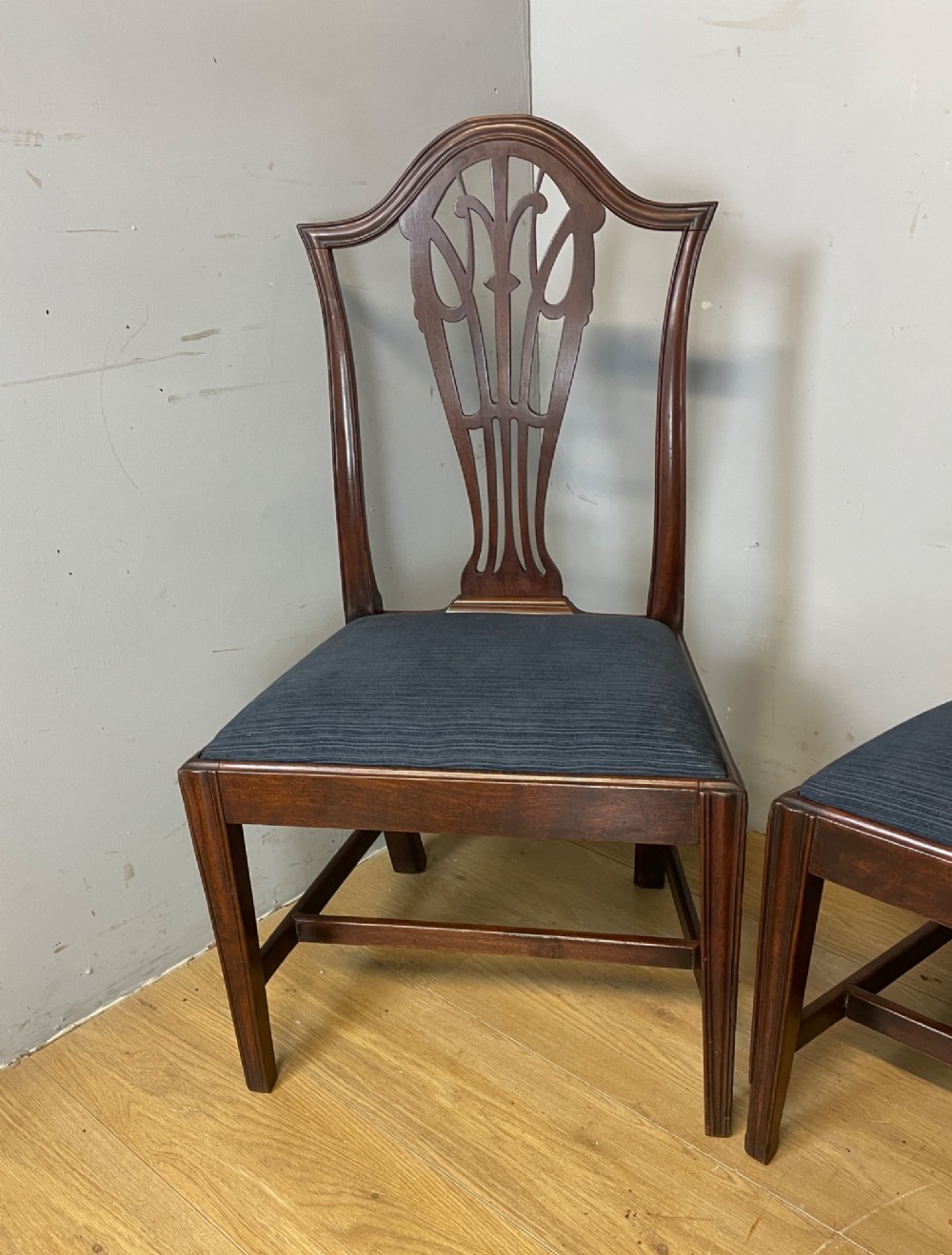 A set of four antique mahogany Chippendale style dining chairs with decorative pierced back splats and dark upholstered seats arranged side by side. View V