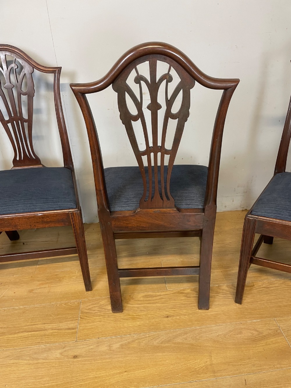 A set of four antique mahogany Chippendale style dining chairs with decorative pierced back splats and dark upholstered seats arranged side by side. View VI