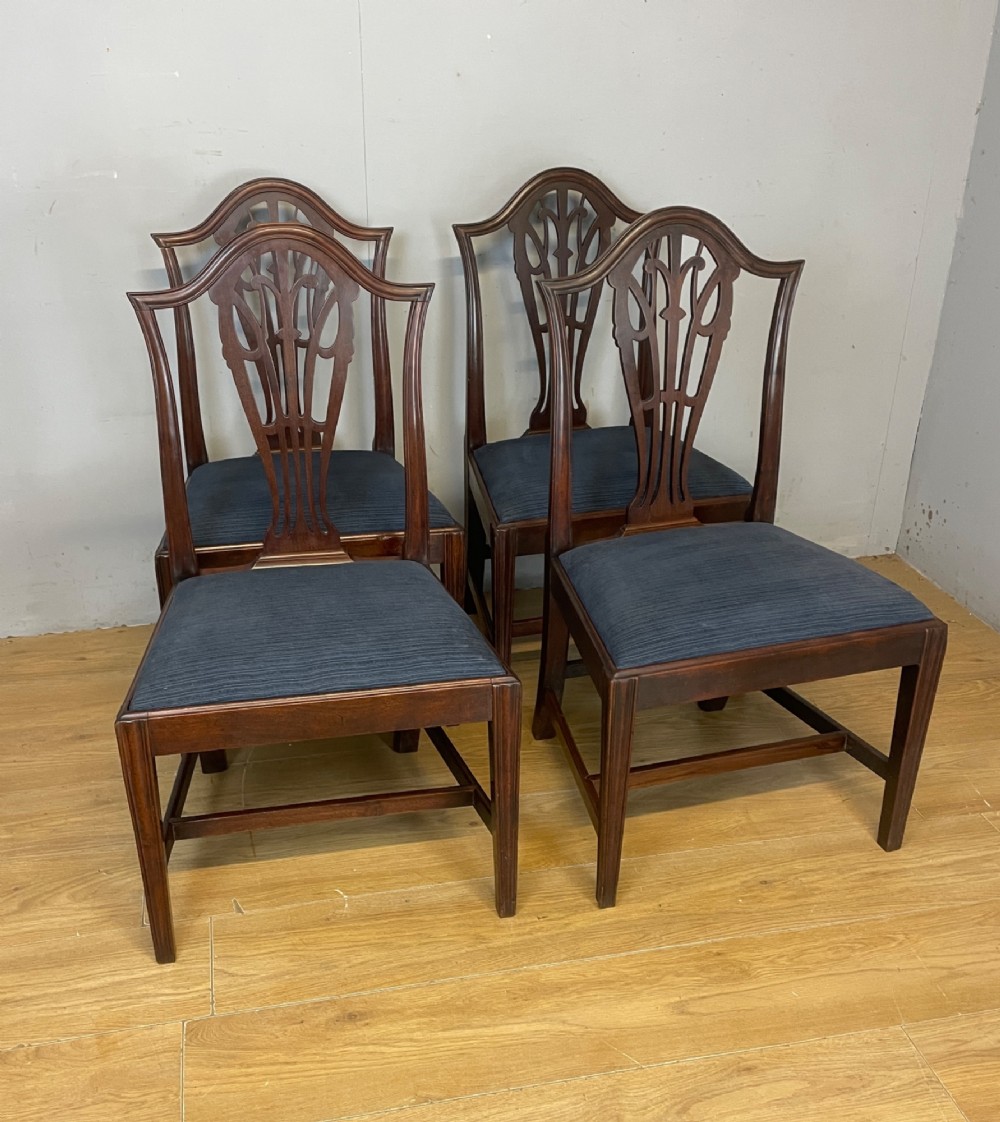 A set of four antique mahogany Chippendale style dining chairs with decorative pierced back splats and dark upholstered seats arranged side by side. View VIII
