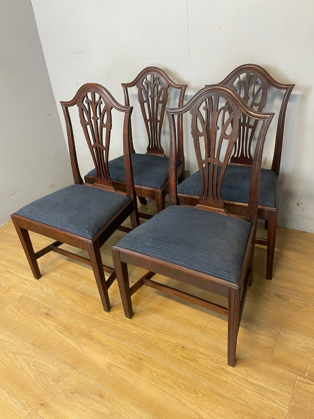 A set of four antique mahogany Chippendale style dining chairs with decorative pierced back splats and dark upholstered seats arranged side by side. View XI