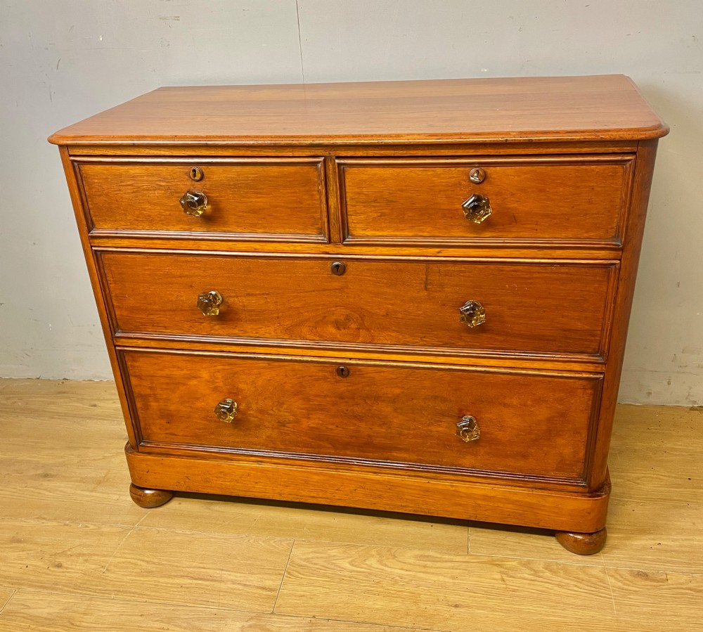 A nineteenth-century solid teak chest of drawers featuring two short drawers over two long drawers, fitted with faceted glass knobs and resting on turned bun feet. View II