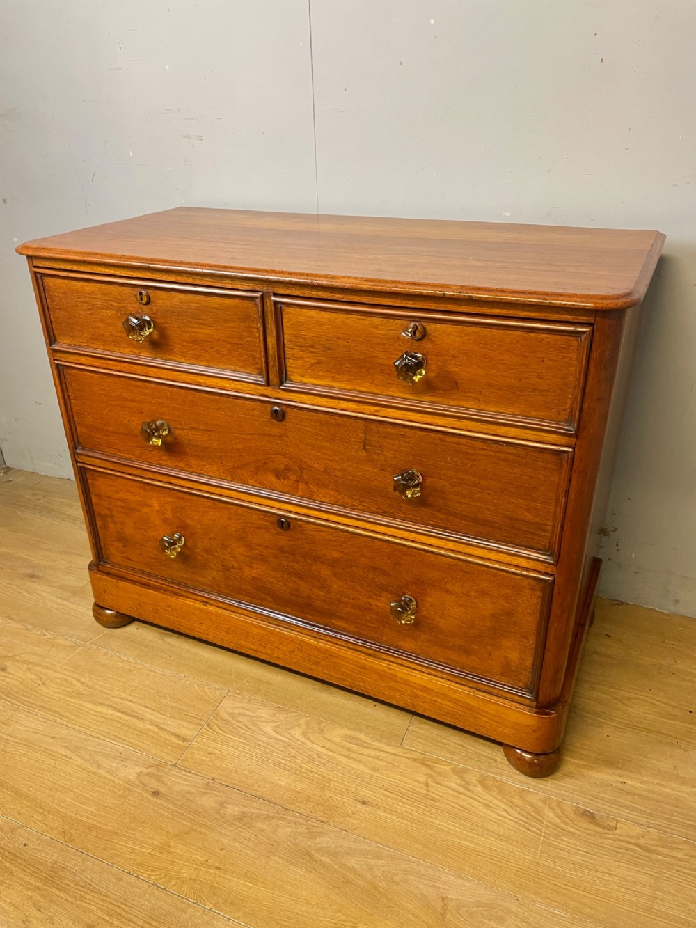 A nineteenth-century solid teak chest of drawers featuring two short drawers over two long drawers, fitted with faceted glass knobs and resting on turned bun feet. View III