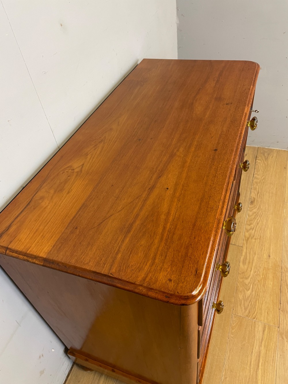 A nineteenth-century solid teak chest of drawers featuring two short drawers over two long drawers, fitted with faceted glass knobs and resting on turned bun feet. View IV