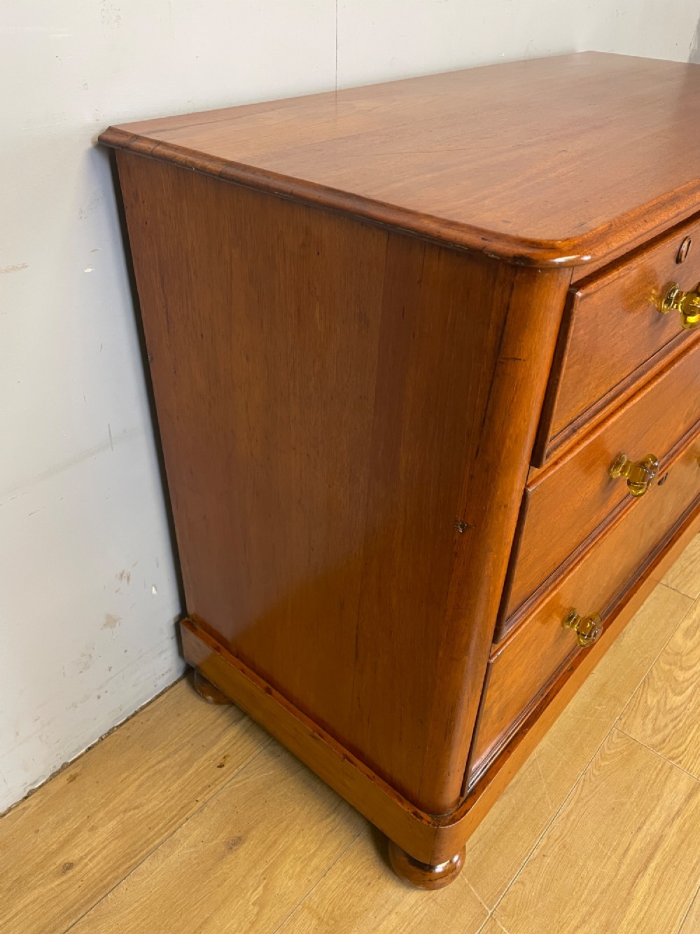 A nineteenth-century solid teak chest of drawers featuring two short drawers over two long drawers, fitted with faceted glass knobs and resting on turned bun feet. View V