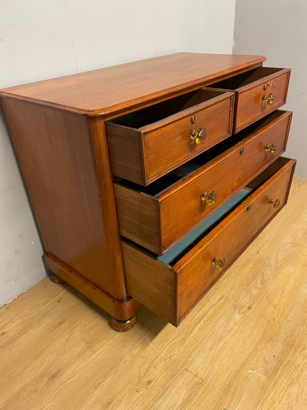 A nineteenth-century solid teak chest of drawers featuring two short drawers over two long drawers, fitted with faceted glass knobs and resting on turned bun feet. View VIII