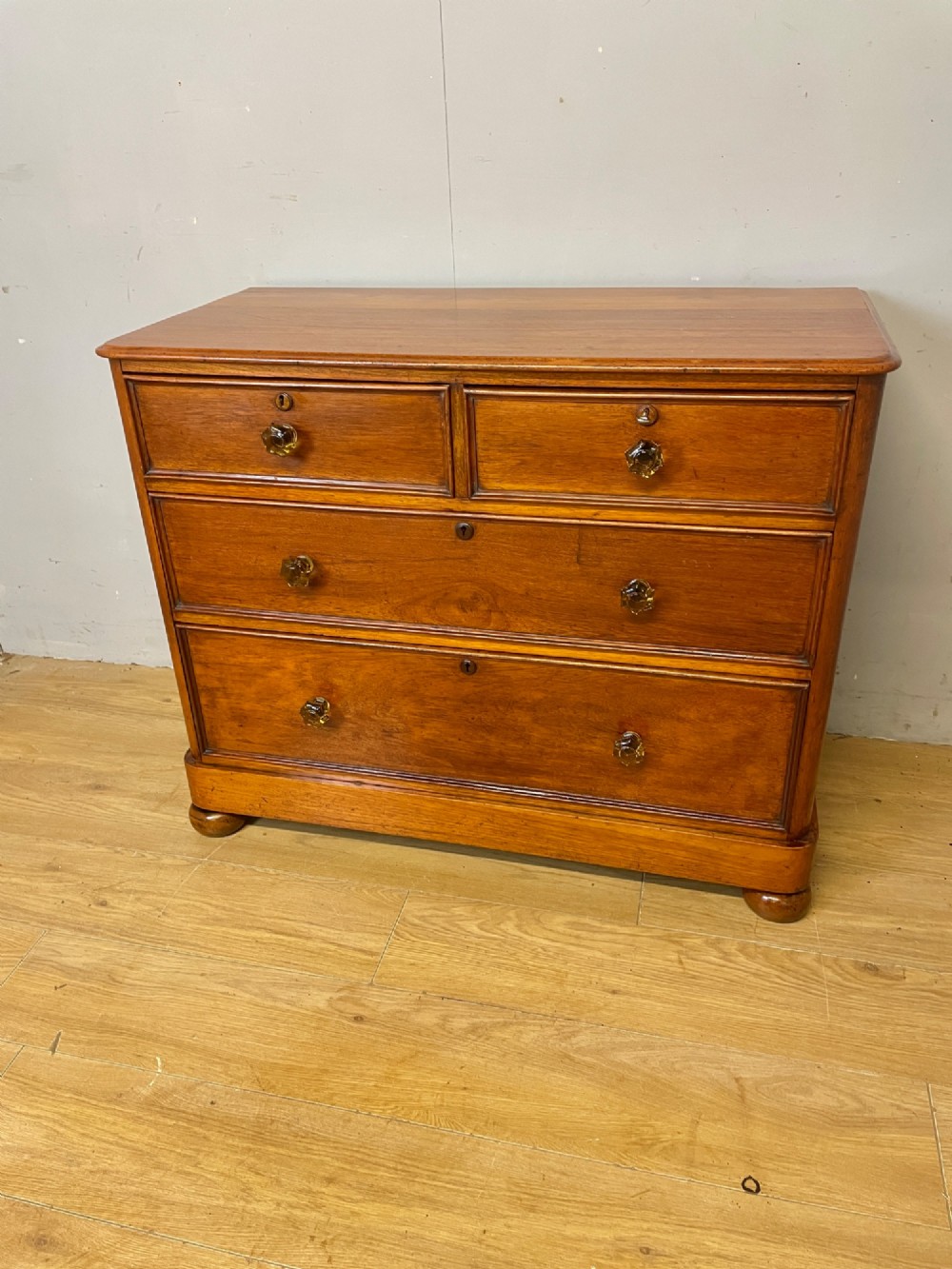 A nineteenth-century solid teak chest of drawers featuring two short drawers over two long drawers, fitted with faceted glass knobs and resting on turned bun feet. View IX