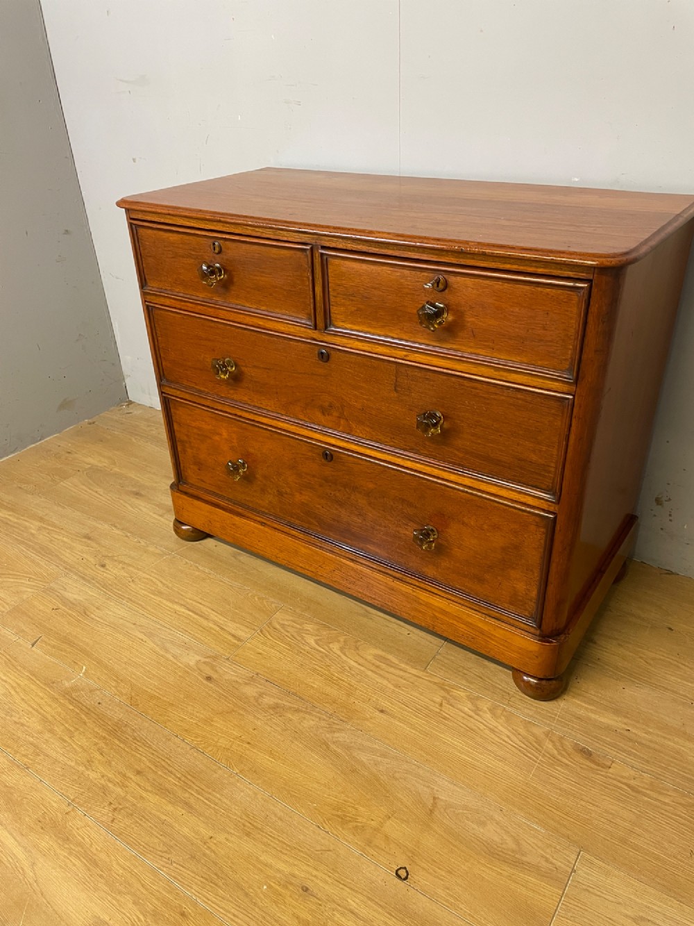 A nineteenth-century solid teak chest of drawers featuring two short drawers over two long drawers, fitted with faceted glass knobs and resting on turned bun feet. View X