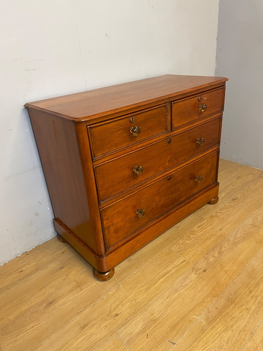 A nineteenth-century solid teak chest of drawers featuring two short drawers over two long drawers, fitted with faceted glass knobs and resting on turned bun feet. View XI