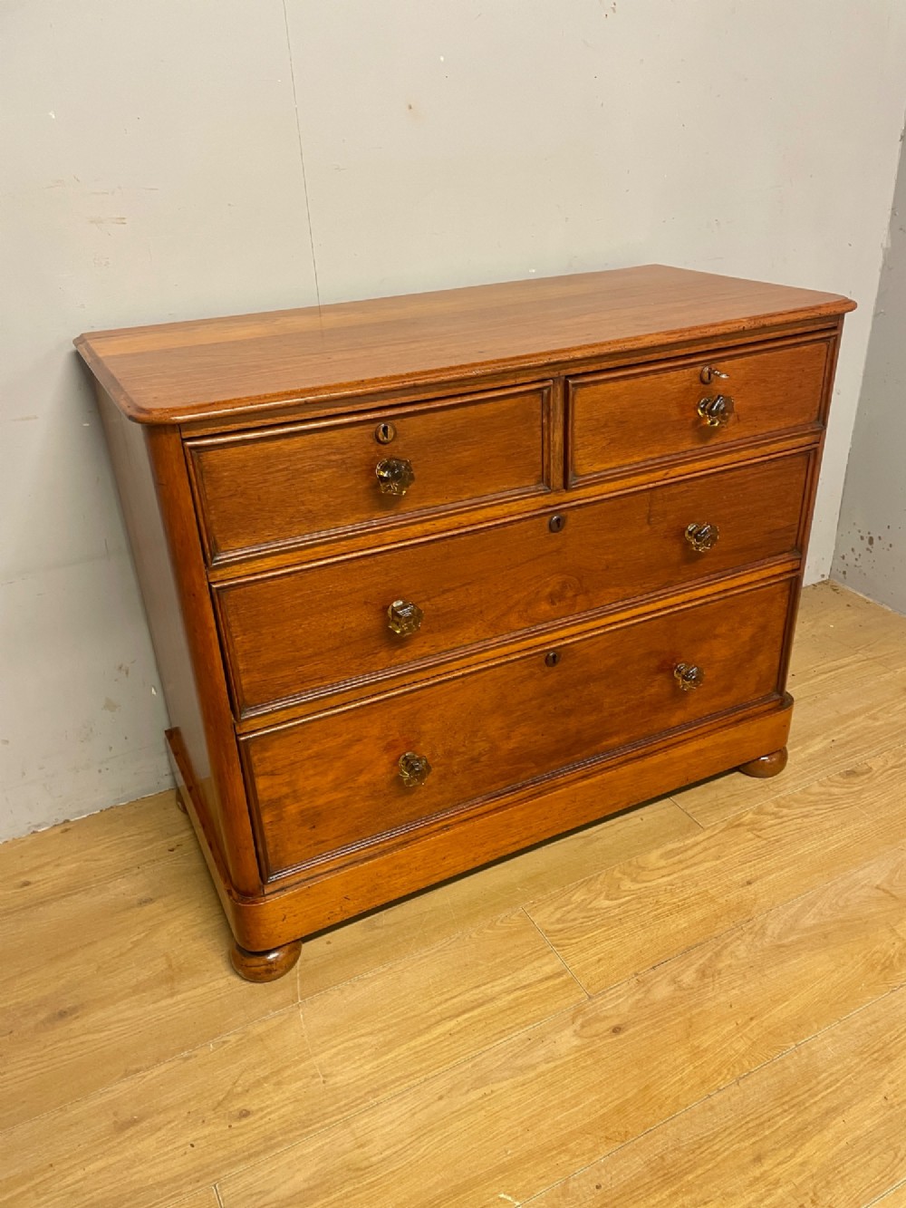 A nineteenth-century solid teak chest of drawers featuring two short drawers over two long drawers, fitted with faceted glass knobs and resting on turned bun feet. View XII