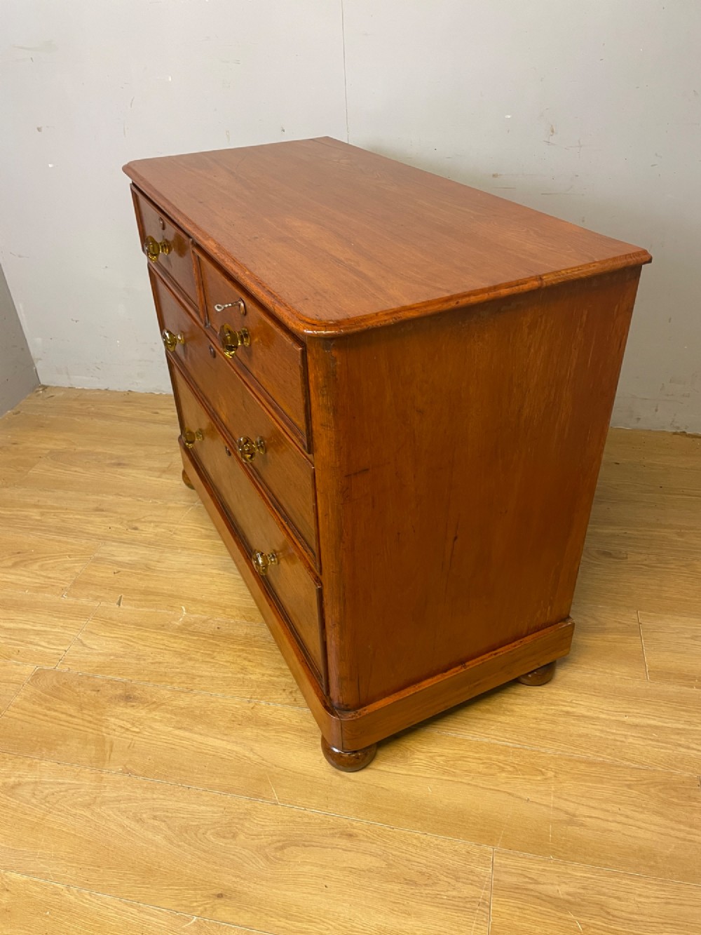 A nineteenth-century solid teak chest of drawers featuring two short drawers over two long drawers, fitted with faceted glass knobs and resting on turned bun feet. View XIV