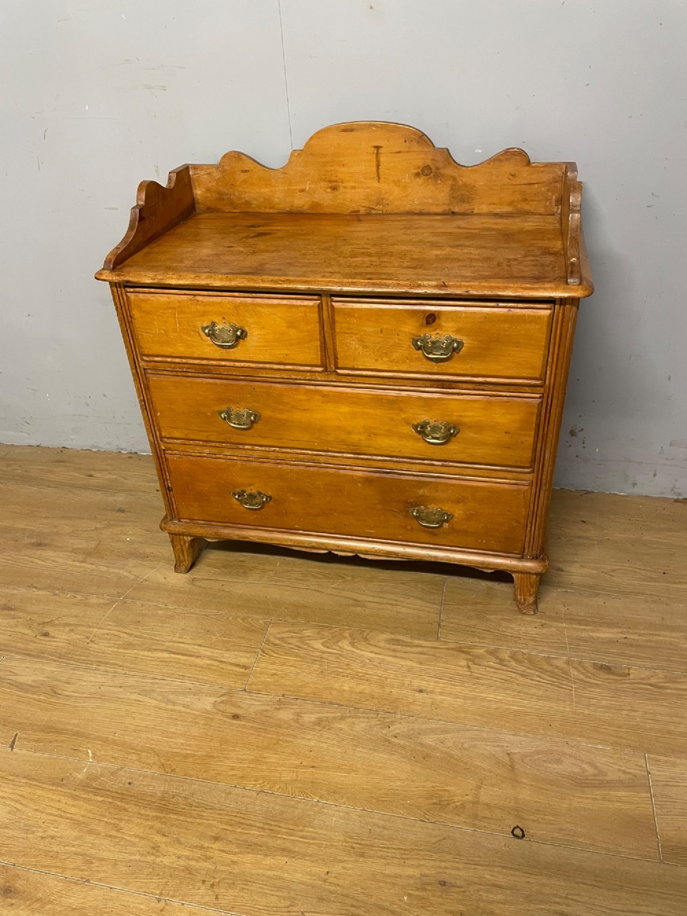 A nineteenth-century warm pine chest of drawers featuring a shaped gallery back, two short over two long drawers, and brass handles.