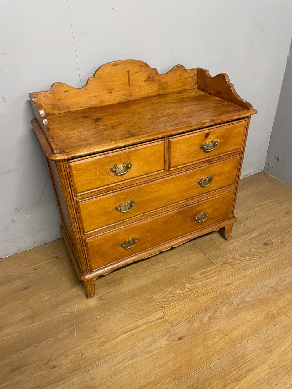 A nineteenth-century warm pine chest of drawers featuring a shaped gallery back, two short over two long drawers, and brass handles. View II