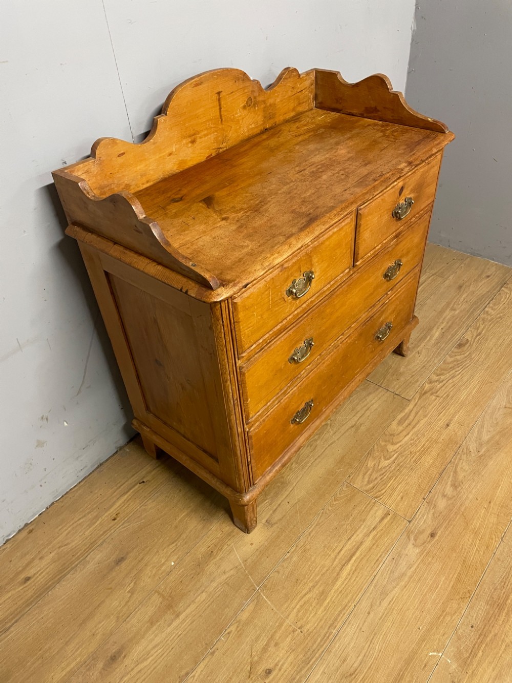 A nineteenth-century warm pine chest of drawers featuring a shaped gallery back, two short over two long drawers, and brass handles. View III