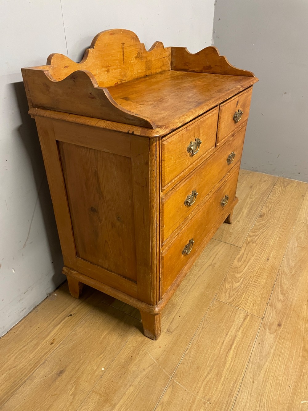 A nineteenth-century warm pine chest of drawers featuring a shaped gallery back, two short over two long drawers, and brass handles. View IV