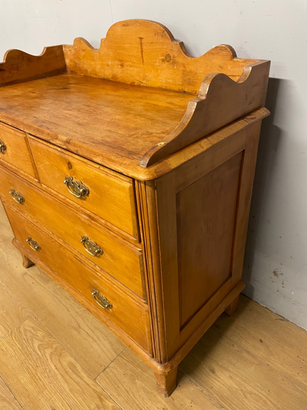 A nineteenth-century warm pine chest of drawers featuring a shaped gallery back, two short over two long drawers, and brass handles. View V