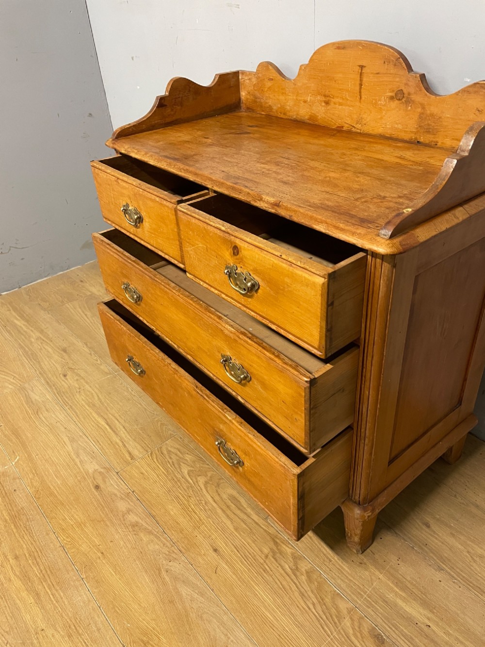 A nineteenth-century warm pine chest of drawers featuring a shaped gallery back, two short over two long drawers, and brass handles. View VI