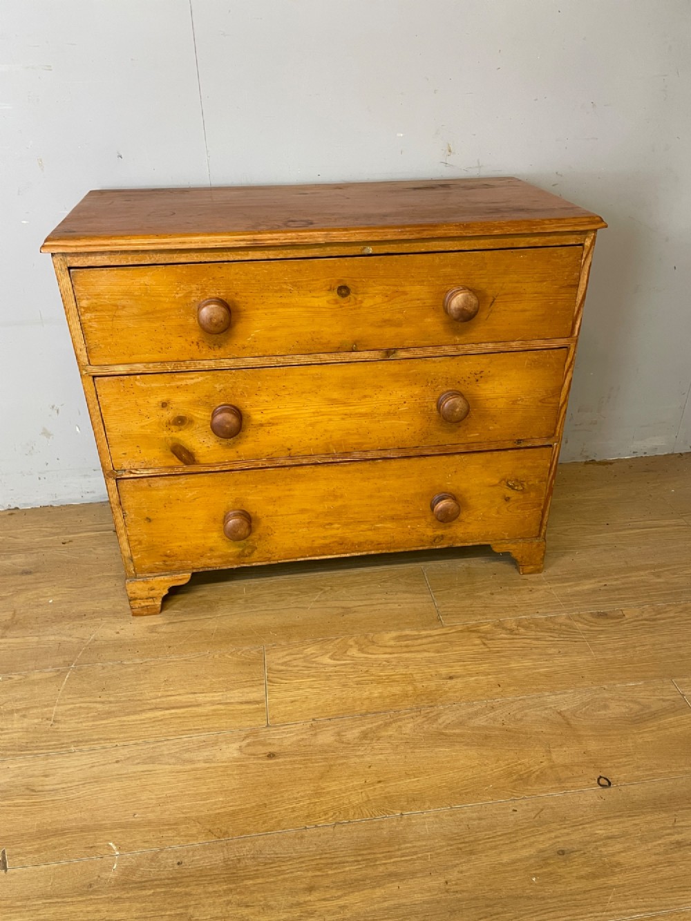 A nineteenth-century pine chest of drawers featuring three full-width drawers with turned wooden handles and bracket feet. View II
