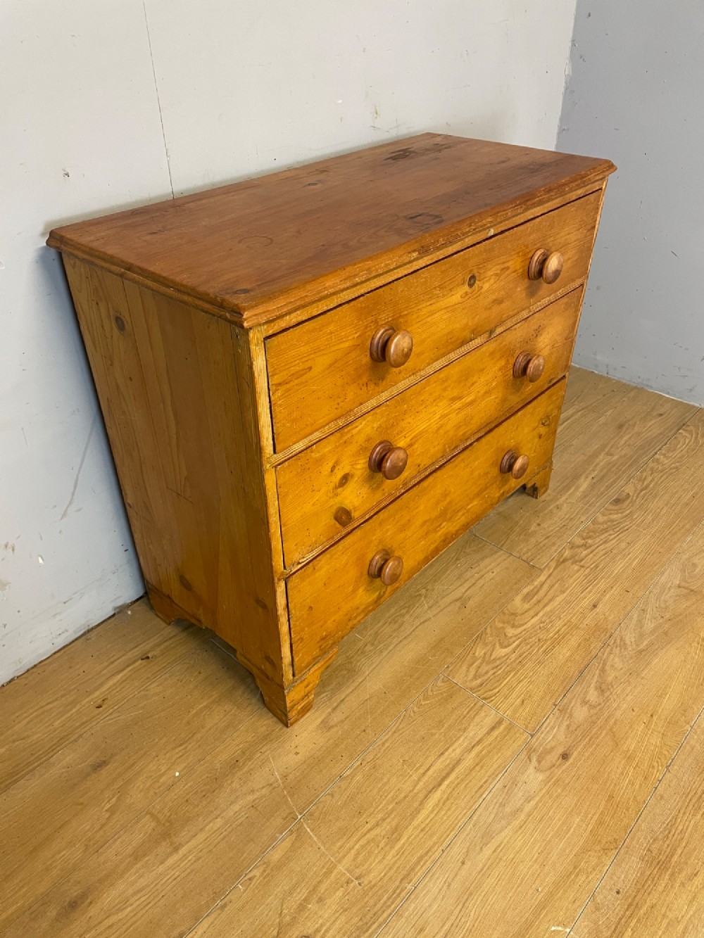 A nineteenth-century pine chest of drawers featuring three full-width drawers with turned wooden handles and bracket feet. View IV